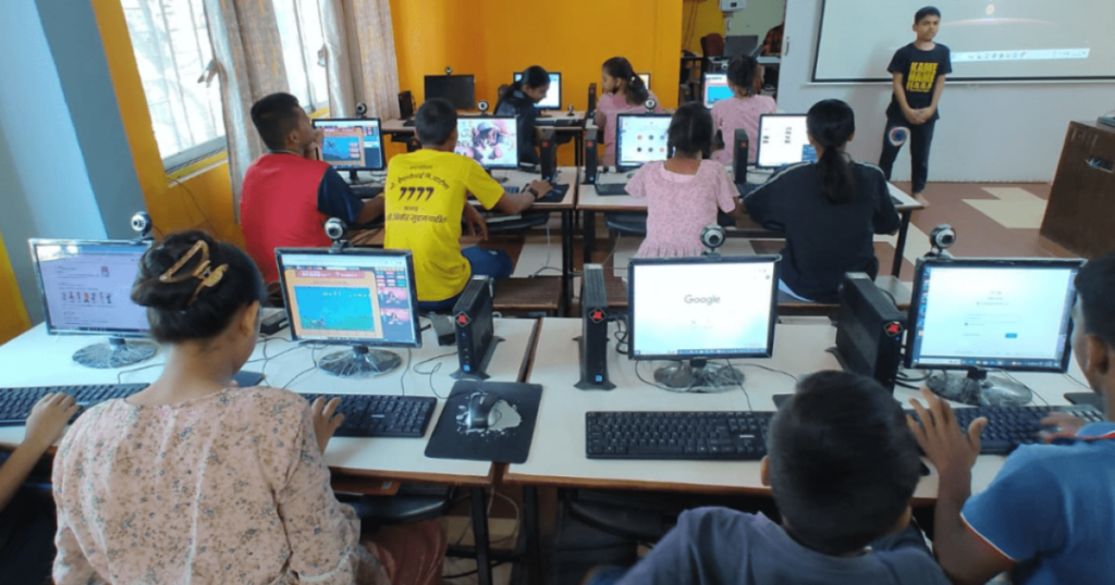 Children in an ApniPathshala learning pod, using laptops and engaging with a digital curriculum projected on a screen in a group setting.